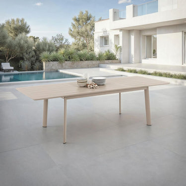 Outdoor dining table with bowls on a patio near a pool and modern house.